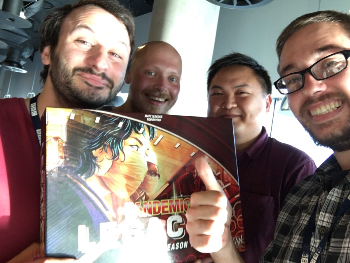 Si and three work friends holding a copy of the boardgame, Pandemic Legacy